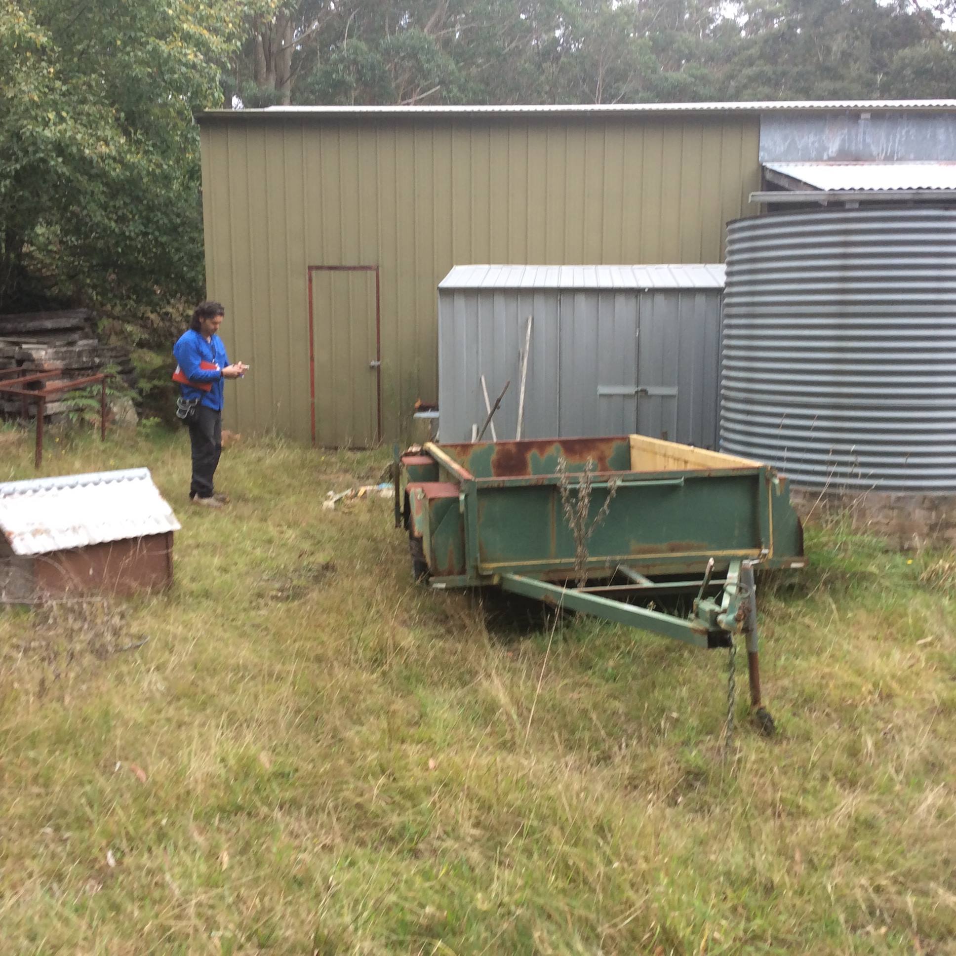A person standing in a yard near a shed and trailer, working on clearing materials, Home improvement