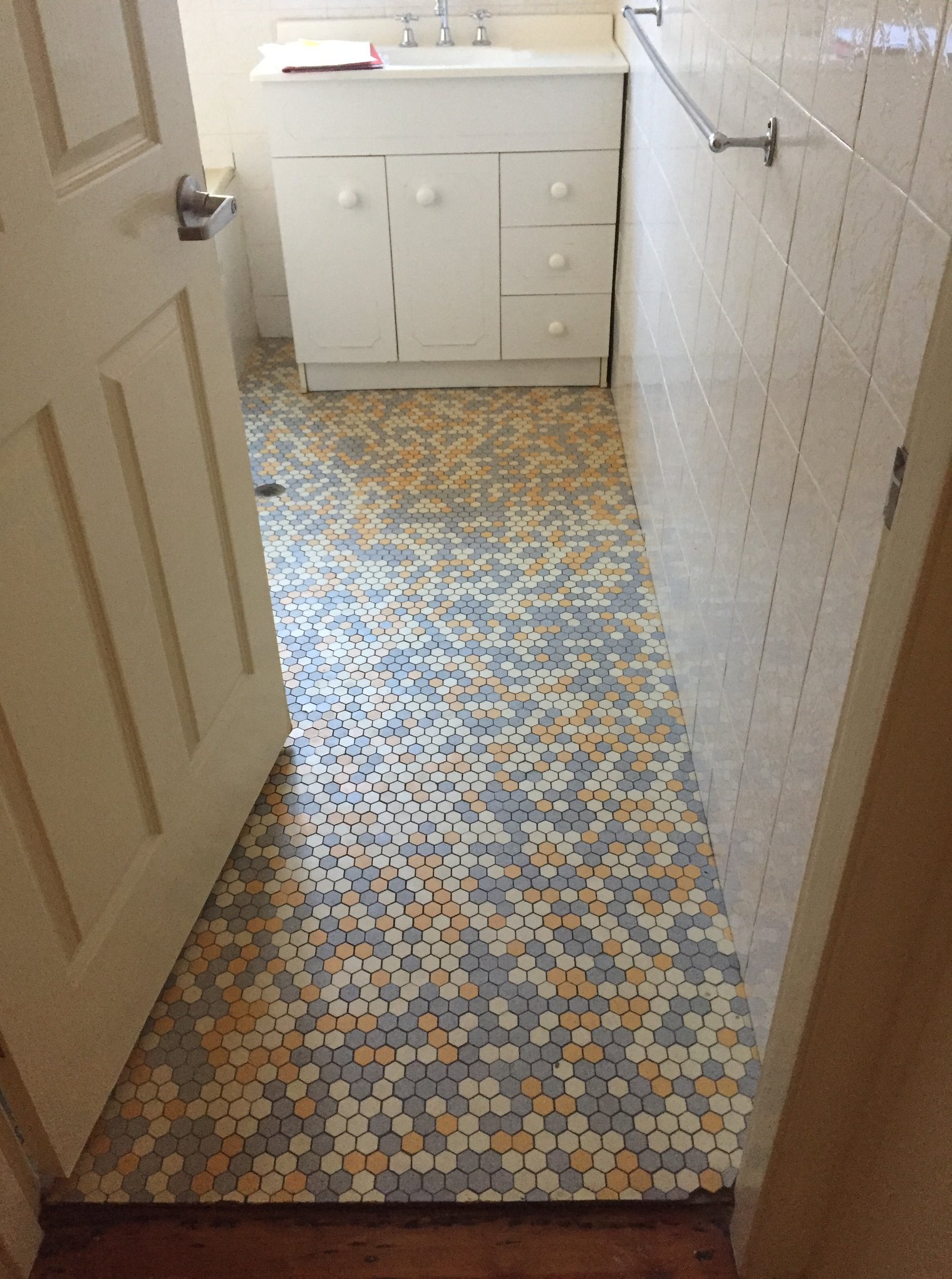 A newly renovated bathroom with a mosaic tiled floor, a white vanity, and a towel rack on the wall.