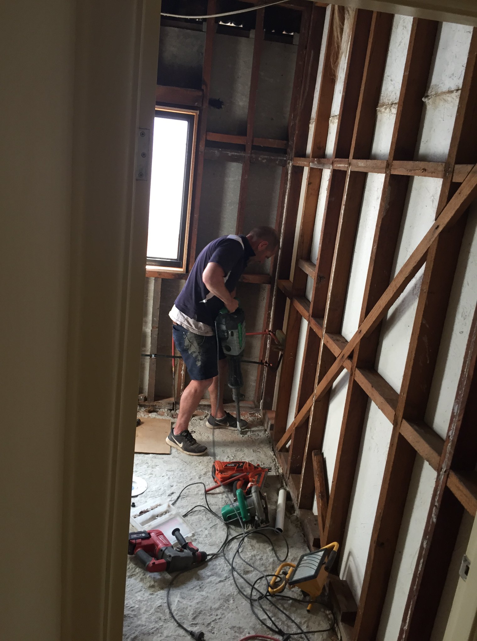 A construction worker working inside a room with exposed walls and electrical wiring.