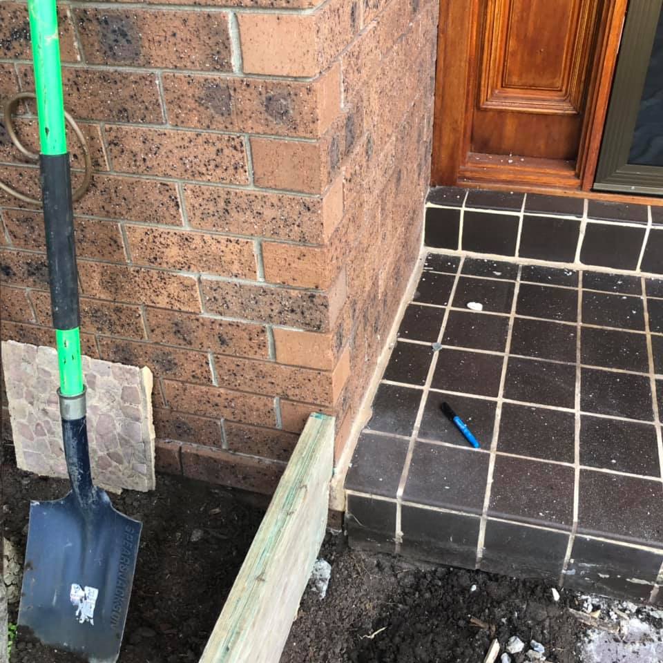  A shovel leaning against a brick wall near a partially dug trench.