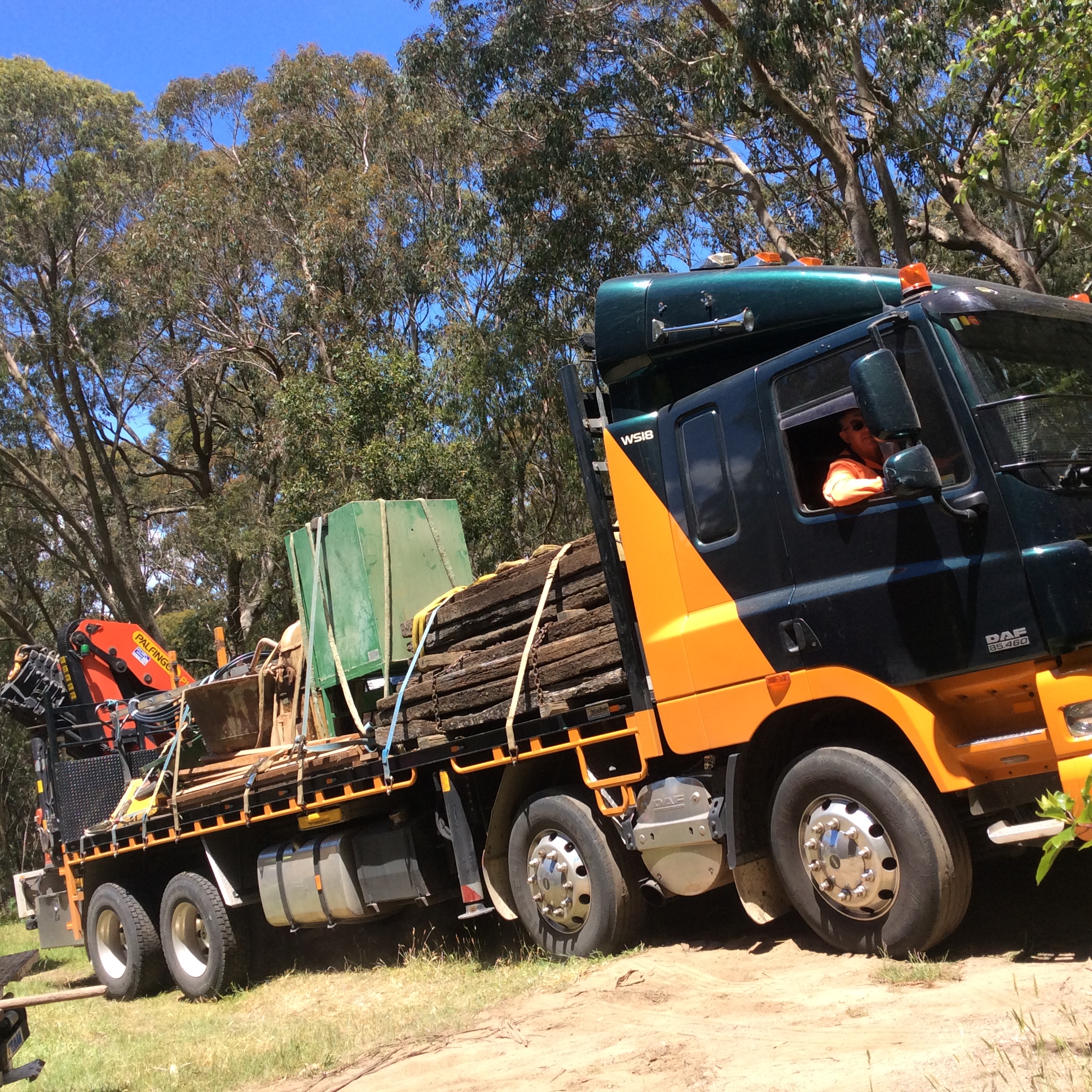 A heavy-duty truck loaded with scrap metal and construction debris, parked near trees.