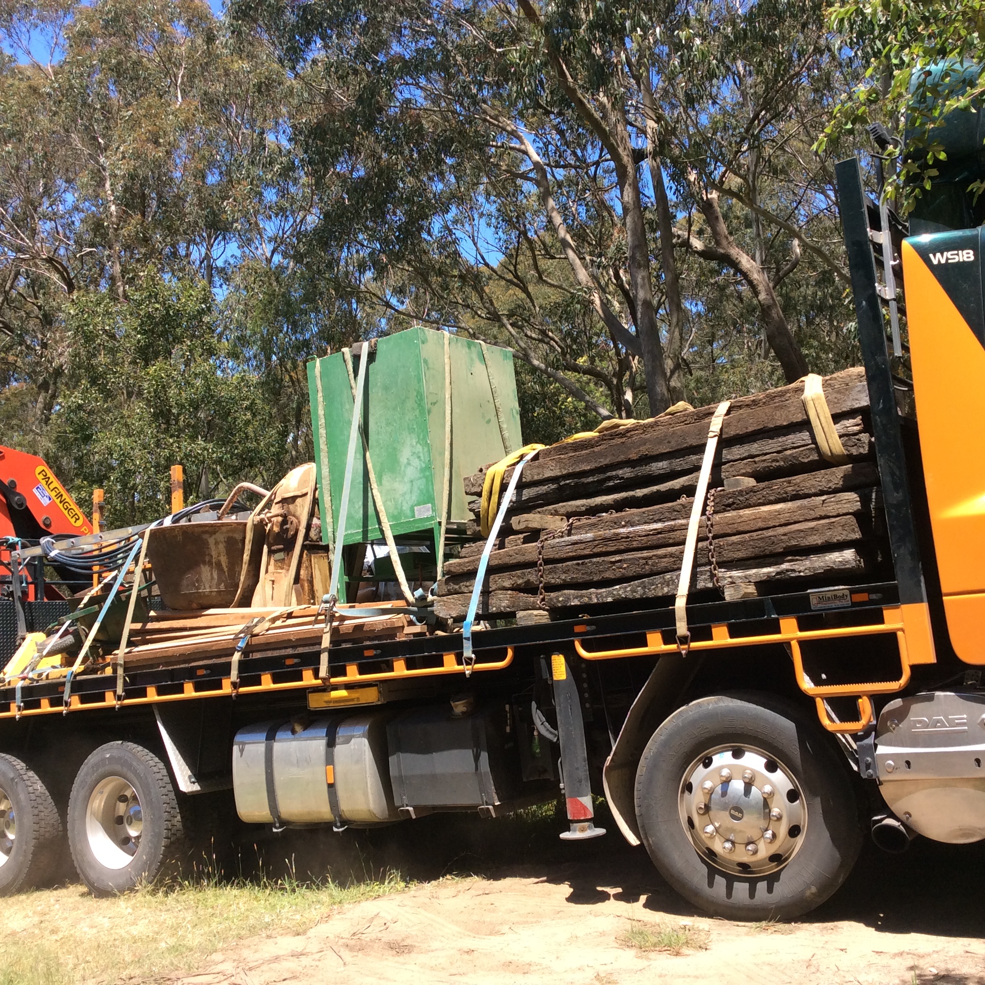 A truck filled with scrap metal and industrial materials, parked in a wooded area.