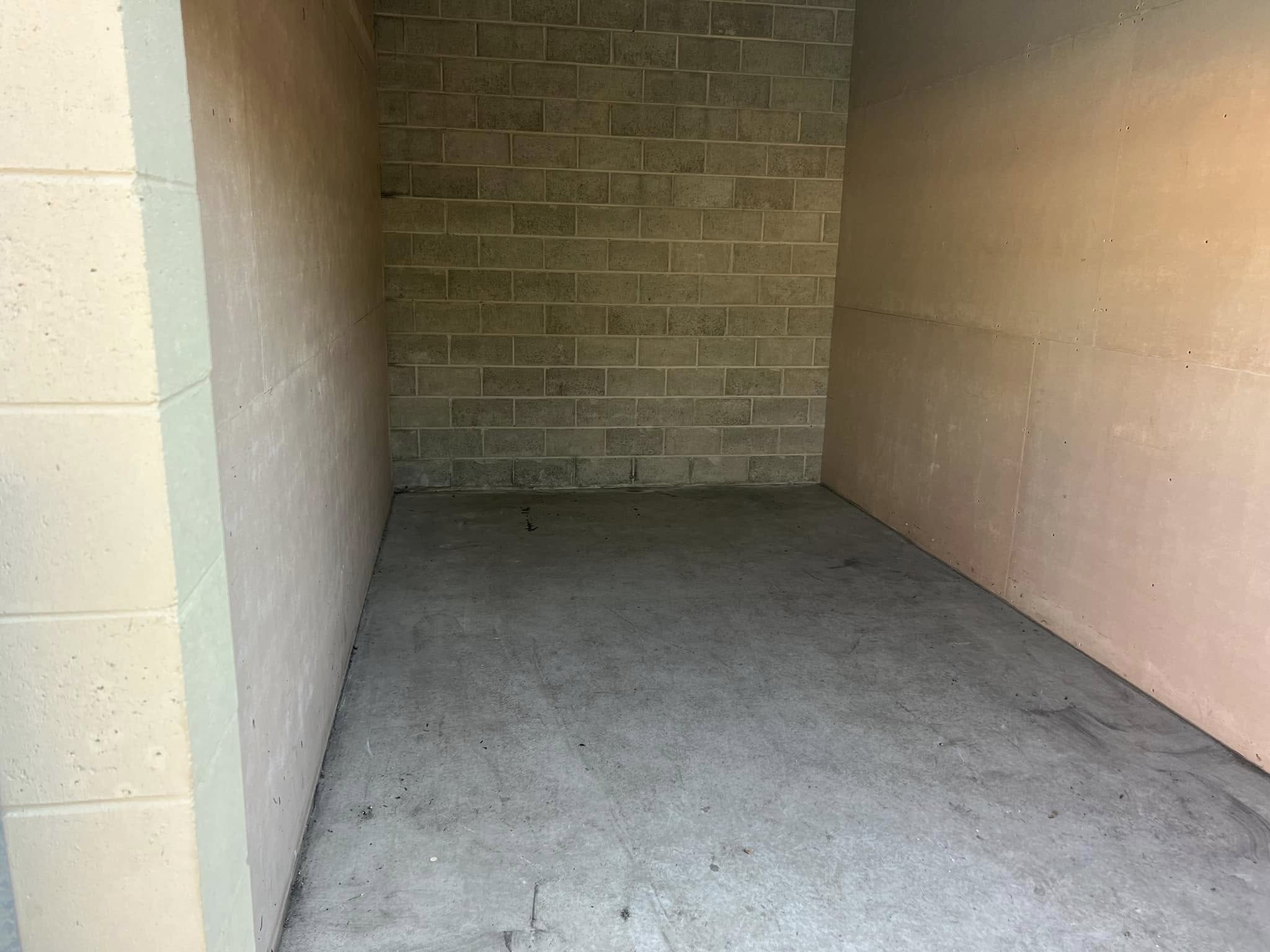 A vacant storage unit with a concrete floor and empty walls.